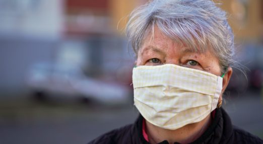 Elderly senior woman wearing home made cloth face mask outside, blurred building background