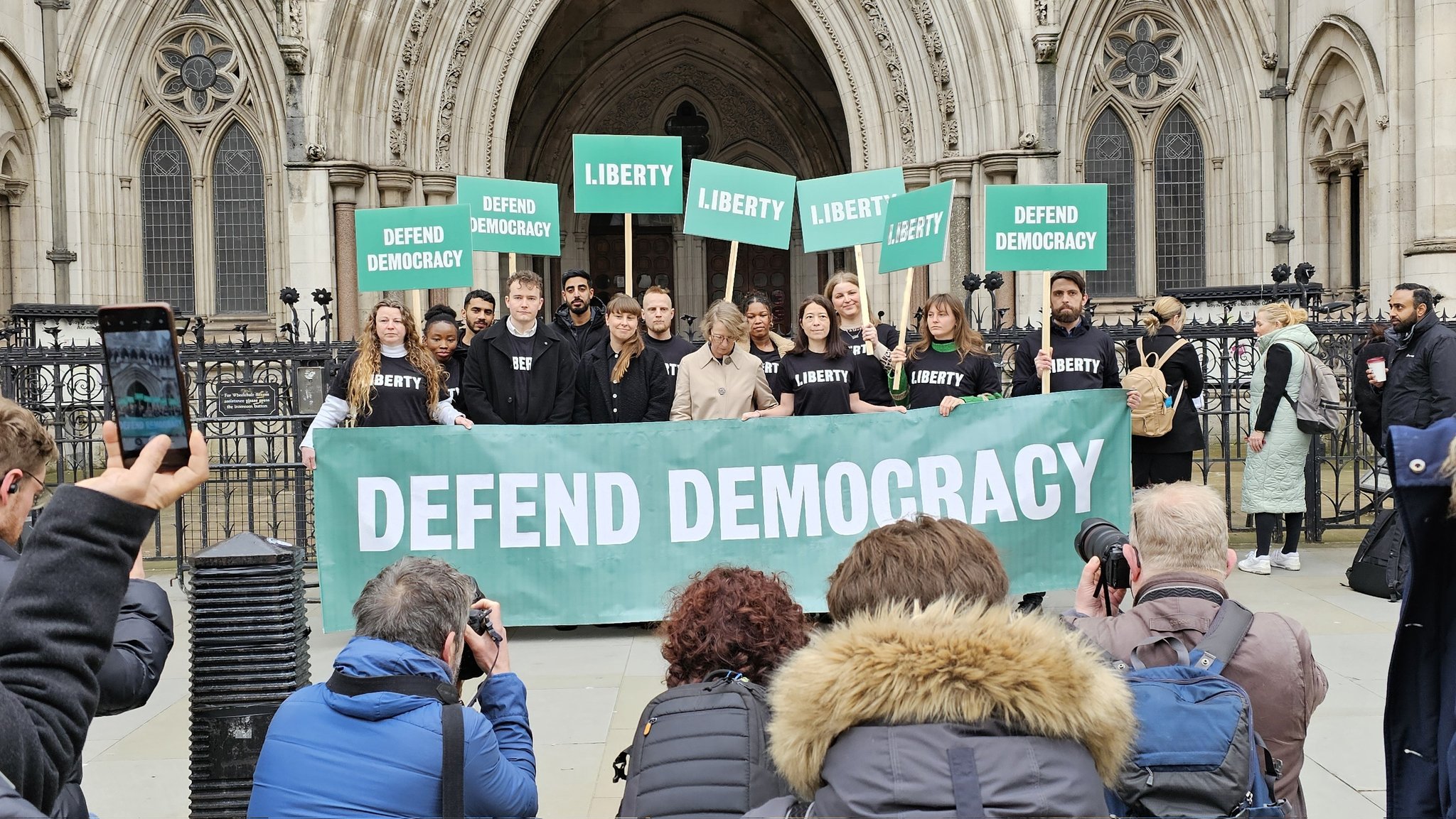 Liberty lawyers and staff outside the Royal Courts of Justice holding a banner that says "DEFEND DEMOCRACY"